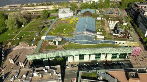 Wide drone view of the University of Warsaw Library garden, featuring green roof design, glass buildings, city streets and modern Warsaw scenery.