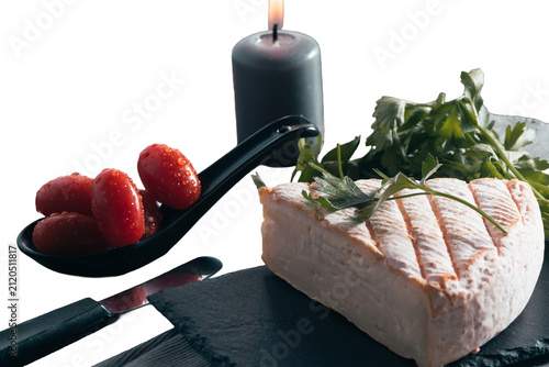 Brie cheese appetizer with fresh tomatoes, parsley, and lit candle on a dark slate board, transparent background