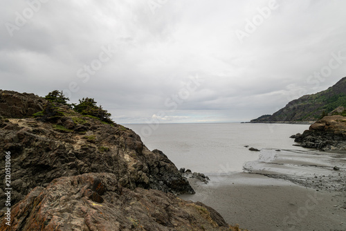 Rugged coastal cliffs framing silty estuary water and sandy beach under overcast sky at Beluga Point Turnagain Arm Anchorage Alaska USA