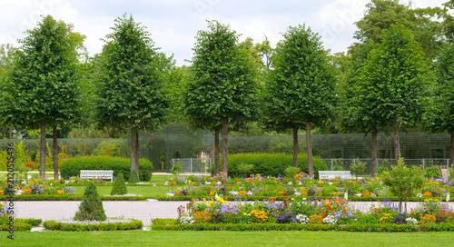 Beautiful formal garden landscape with manicured trees, blooming flowers, and white benches.