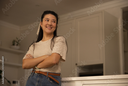 African American or Asian woman in striped shirt leaning on kitchen counter, smiling, looking right