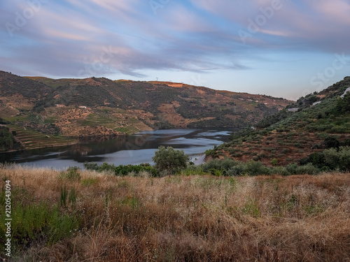 Idyllic view of the Tua River surrounded by vineyards, olive trees and rugged hills in São Mamede de Ribatua, Alijó, Portugal, at sunset.