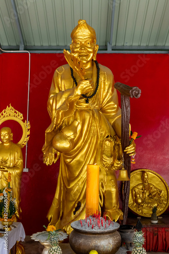 Bild auf Leinwand Gleaming golden statue of Guanyin or similar deity in ornate robes, holding ritual items and surrounded by offerings