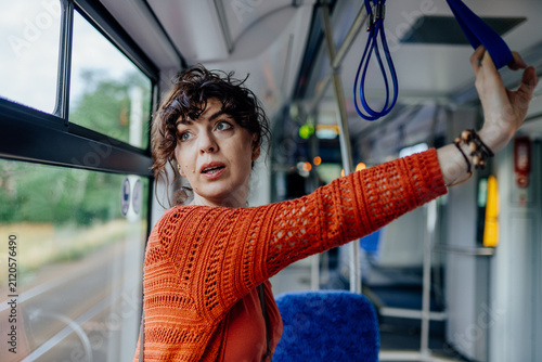 Canvastavla Surprised young woman holding overhead strap while traveling by public tram