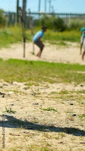 Vertical video: Stepping off peg, barefoot teen green-top kicking ball to play on sand, copy space