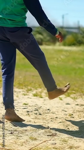 Vertical video: Cam zooming kid in green top hopping on sandy lot near stake and showing wristbands