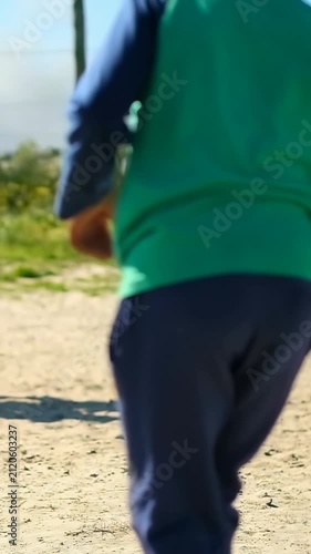 Vertical video: Spotting sandal and ball, barefoot kid in green top blue pants nudging ball on path