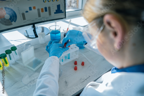 A researcher precisely transfers blue liquid into test tubes, focusing on scientific analysis. Laboratory glassware, digital charts, and a clean workspace highlight advanced research methods