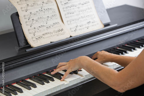 Woman playing digital piano while reading vintage sheet music during music practice. Close-up of female hands playing a digital piano with aged sheet music on the music stand. 