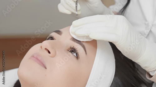Close up of a cosmetologist performing a facial extraction procedure on a client’s forehead, focusing on clear skin and hygiene. The scene highlights modern skincare and beauty trends