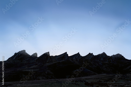 Jagged dark mountain ridge silhouetted against a soft blue twilight sky at dusk