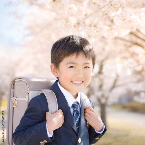 Smiling Japanese boy with randoseru backpack on first day of school under cherry blossoms