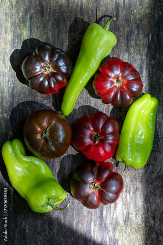 Heirloom tomatoes and green sweet peppers on dark rustic wooden background, flat lay
