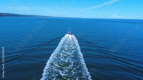 A fishing boat moves across the wide St. Lawrence River, its wake stretching behind in the still water.