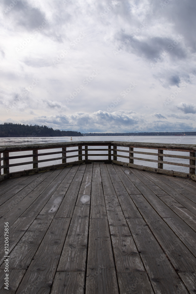 Obraz premium Wooden pier balcony extending toward calm water under dramatic skies in Vancouver, British Columbia