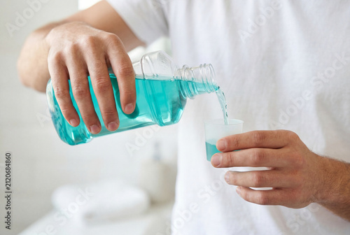 Man pouring blue mouthwash into measuring cup in bright bathroom