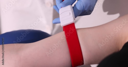 Doctor applying medical tourniquet on patient's arm indoors, closeup