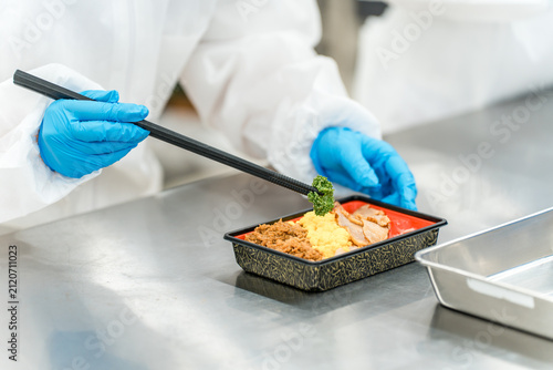 Fotografie A food factory staff member is shown assembling bento boxes in the kitchen (food factory, food processing, food hygiene)
