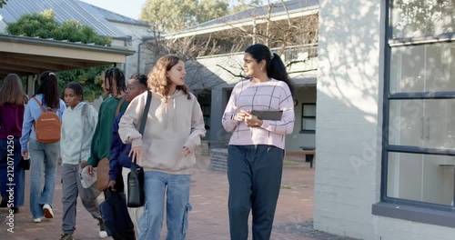 Two teen girls entering from left walking in courtyard, left speaking, Indian girl holding tablet