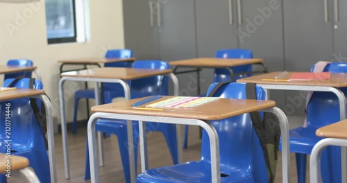 Shot start, camera is shifting, angling to frame front row desk, showing classroom ready for lesson