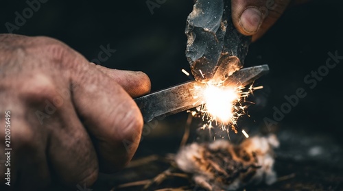 Close up of hands striking a flint and steel to create sparks for fire starting.