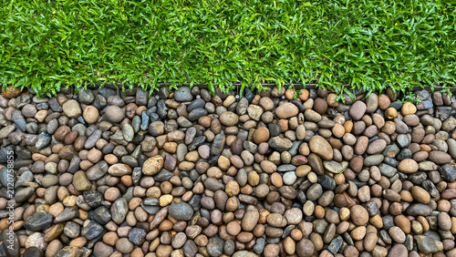 Aerial view of decorative river pebbles and a green lawn separated by a metal border. A textured natural backdrop for landscape design, greening, and landscaping.