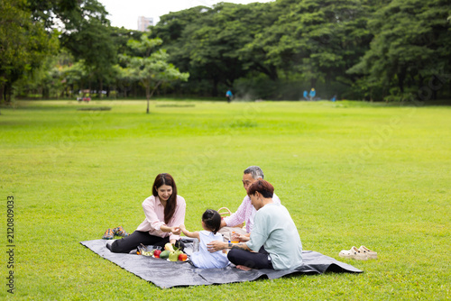 Happy Asian family having fun time on picnic at city nature park sunny day, outdoor activitie with daughter father, mother and grandfather