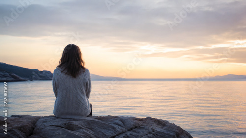 夕暮れの海を見つめる女性の後ろ姿