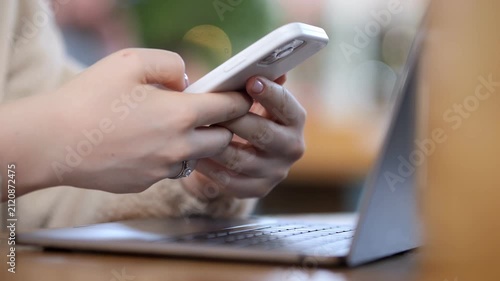 Hands hold phone near laptop. Person multitasks. Focus on digital devices. Work or communication concept. Suitable for tech, productivity, or modern lifestyle themes