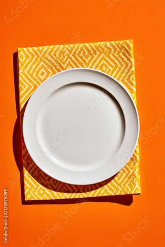 White ceramic plate resting on yellow patterned napkin over orange background in a minimalist top view for restaurant branding and culinary marketing