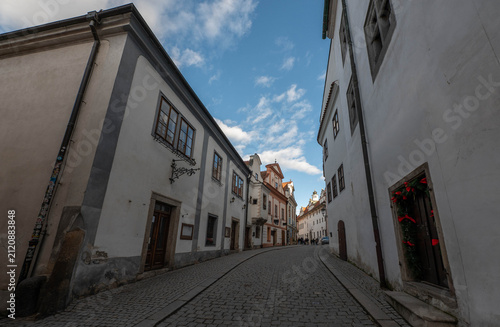 picturesque narrow historic street with traditional white buildings and cobblestone pavement under a bright blue sky with fluffy clouds in a charming European old town