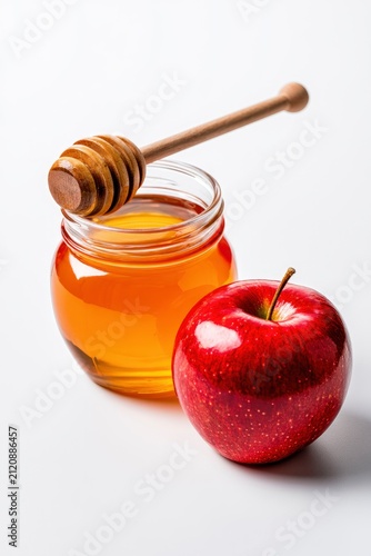 Honey jar with dipper and red apple resting on white background in sharp focus for rosh hashanah holiday marketing