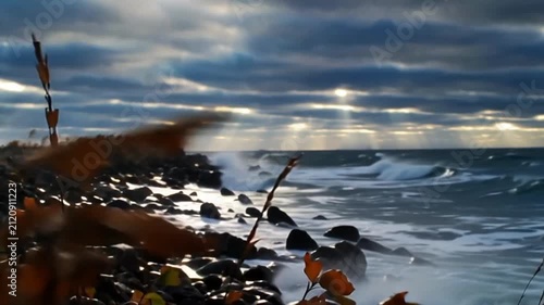 Dramatic ocean waves crashing against a rocky shore under dark stormy clouds with bright sunbeams breaking through the sky in autumn