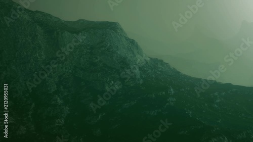 Fog covers the mountains early in the morning. The landscape appears mysterious and quiet as the light filters through the mist. A sense of stillness surrounds the scene.