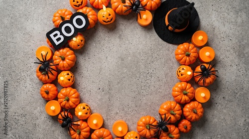 A festive halloween wreath made of small orange pumpkins with a boo sign and witch hat decoration