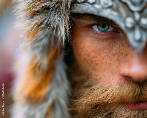 Extreme close-up portrait of a fierce Nordic viking warrior with striking blue eyes, wearing a detailed metal helmet and textured fur hat