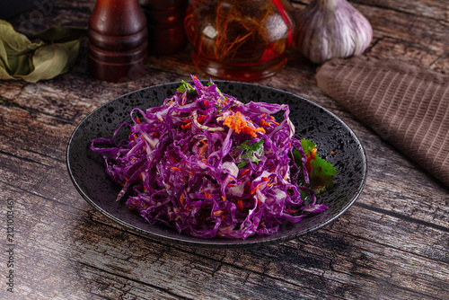 Fresh red cabbage salad with carrot in black bowl on wooden table
