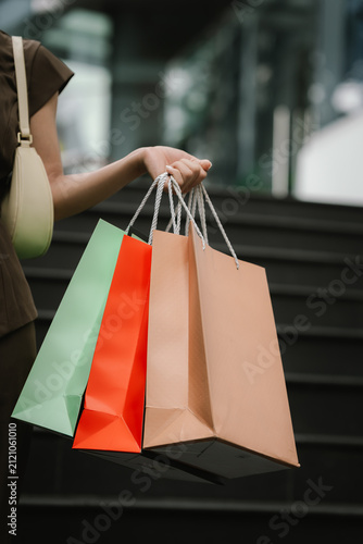 Close-up of a woman carrying colorful shopping bags outside a modern shopping mall, representing retail, consumer lifestyle, fashion, and successful shopping.