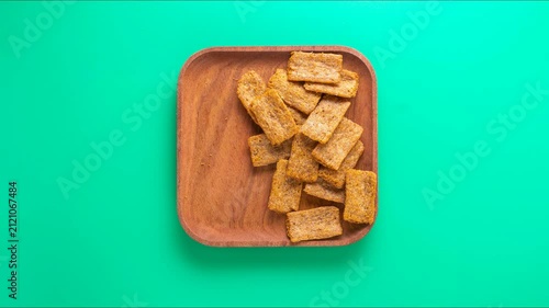 Stopmotion: eating spicy crackers from a wooden plate. Top view, green background