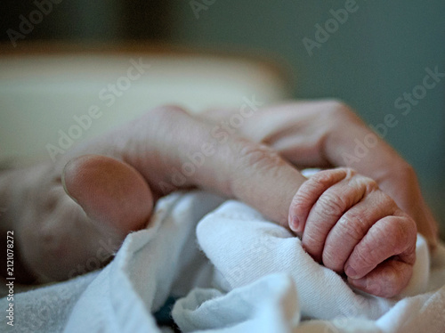 Newborn baby hand tightly grips a parent's finger