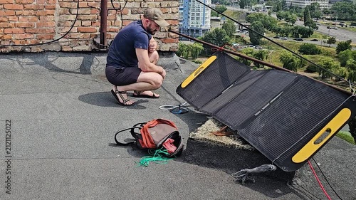 Man Setting Up Portable Foldable Solar Panel on Flat Roof for Alternative Energy