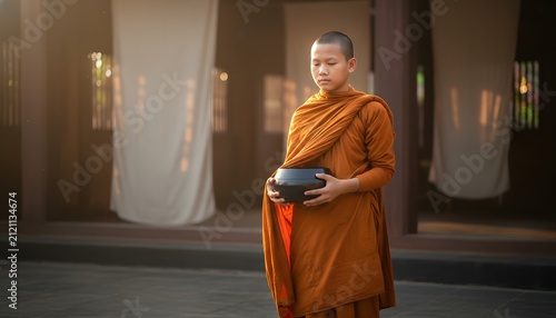 A young buddhist novice monk holding an alms bowl in peaceful meditation during Poson Poya festival for spirituality and religious devotion concept with warm light
