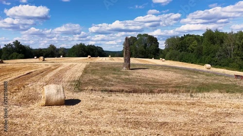 Prähistorischer Gollenstein-Menhir auf einer Wiese bei sommerlicher Erntezeit mit Strohballen unter blauem Wolkenhimmel. Altes Kulturdenkmal in Mitteleuropa.