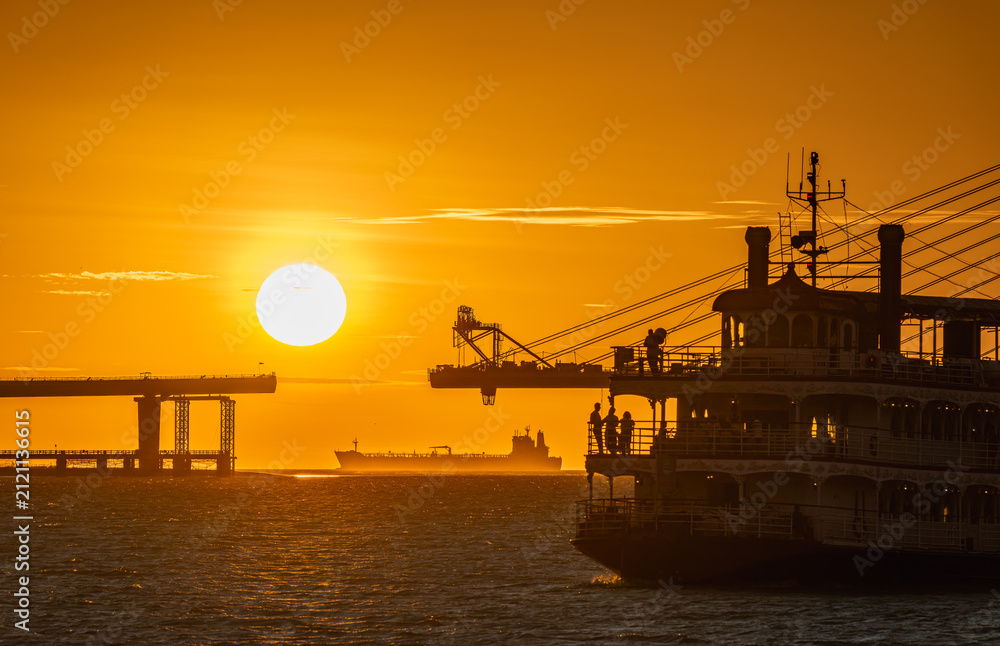 Fototapeta premium A beautiful sunset view featuring the silhouette of a ferry boat and the construction of the Danjiang Bridge in Tamsui, New Taipei City, Taiwan.