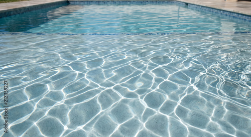 Crystal clear blue swimming pool water with shimmering sunlight, gentle ripples and copy space, ideal for summer vacation, resort, wellness, spa and luxury travel designs.