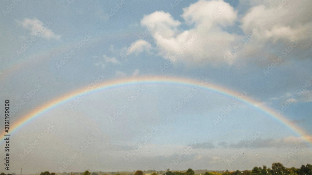 Obraz premium A vibrant double rainbow arching across a soft blue sky with fluffy white clouds above nature