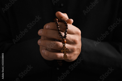 Canvas Print Priest with rosary praying on black background, closeup