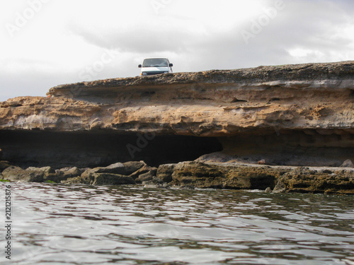 There's a van parked right at the edge of a small cliff by the sea.