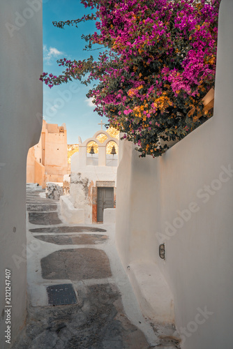 Whitewashed winding alley leading to a traditional bell tower under a bright summer sky