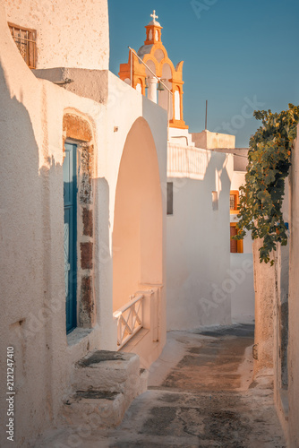 Winding street in a traditional greek village with white cycladic architecture and a church